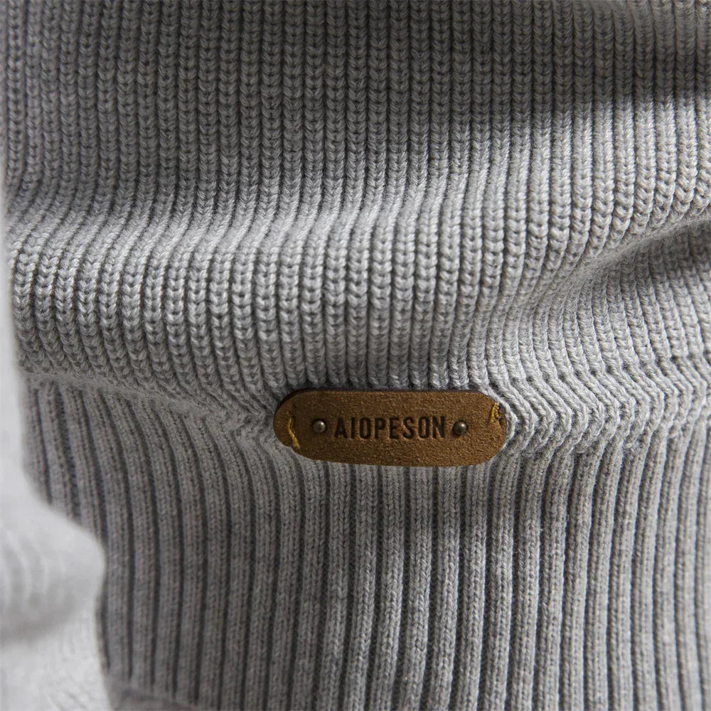 Close-up of a gray knitted sweater with a brown leather label on a white background