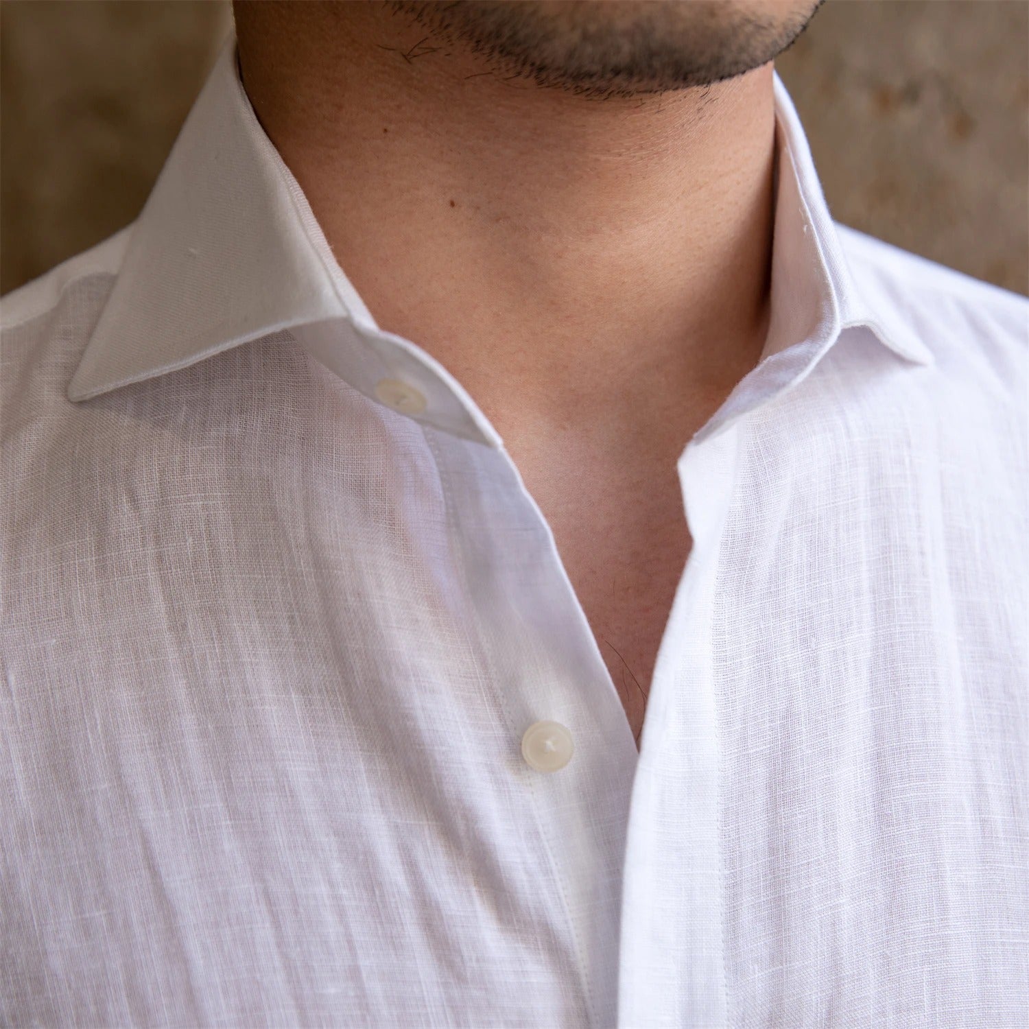 Close-up of a person wearing a white linen shirt with a neutral background