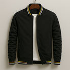 Black bomber jacket with yellow accents on a hanger against a beige background