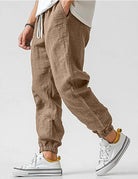 Brown jogger pants worn with white sneakers on a plain background
