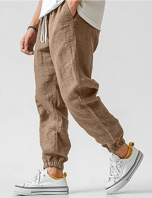 Brown jogger pants worn with white sneakers on a plain background