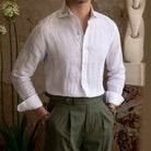 Person wearing a white linen shirt and green pants in an indoor setting with plants and a statue.