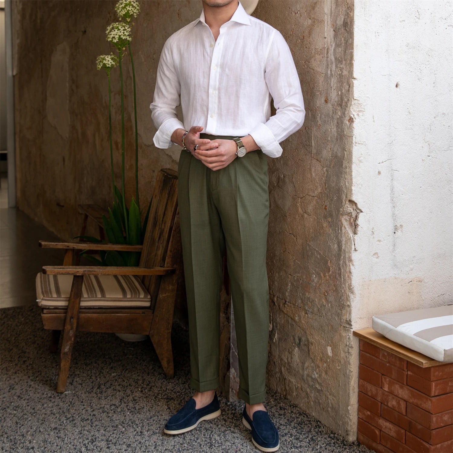 Man wearing a white linen shirt and green pants standing against a textured wall.