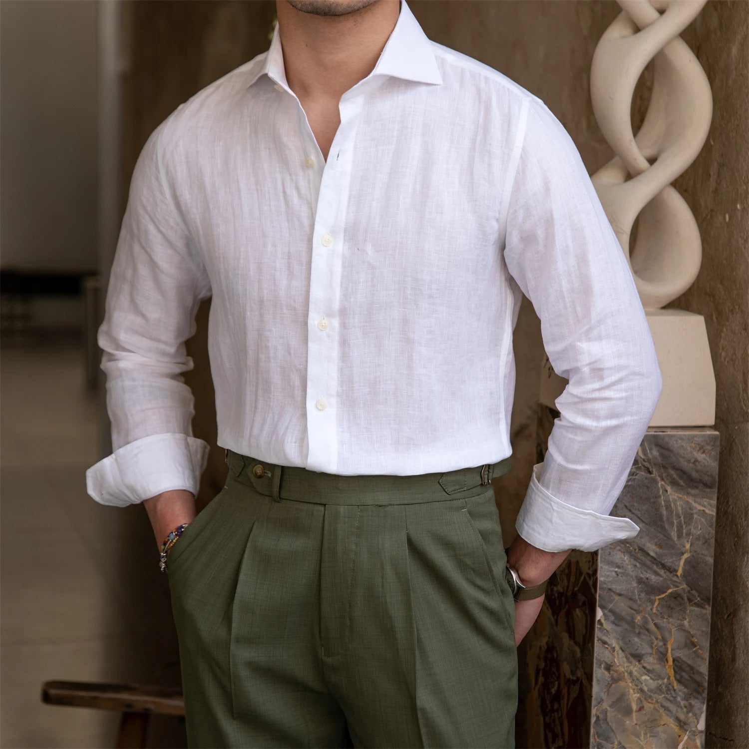 Person wearing a white linen shirt and green pants in an indoor setting.