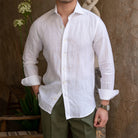 Man wearing a white linen shirt with rolled-up sleeves against a textured wall.