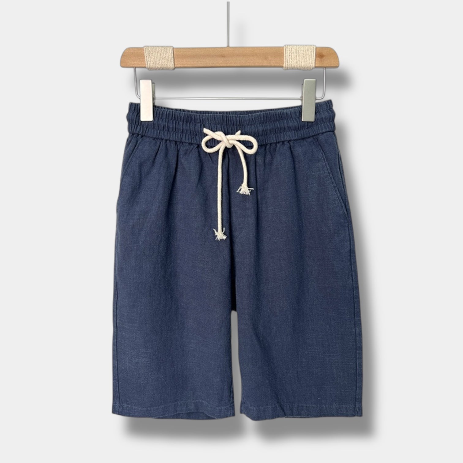 Blue linen shorts with a drawstring on a hanger against a white background