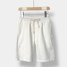 White linen shorts with a drawstring on a wooden hanger against a white background