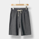 Gray linen shorts with a drawstring on a wooden hanger against a white background