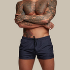 Person wearing navy blue swim shorts with a beige background