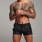 Man with tattoos wearing black swim shorts against a grey background