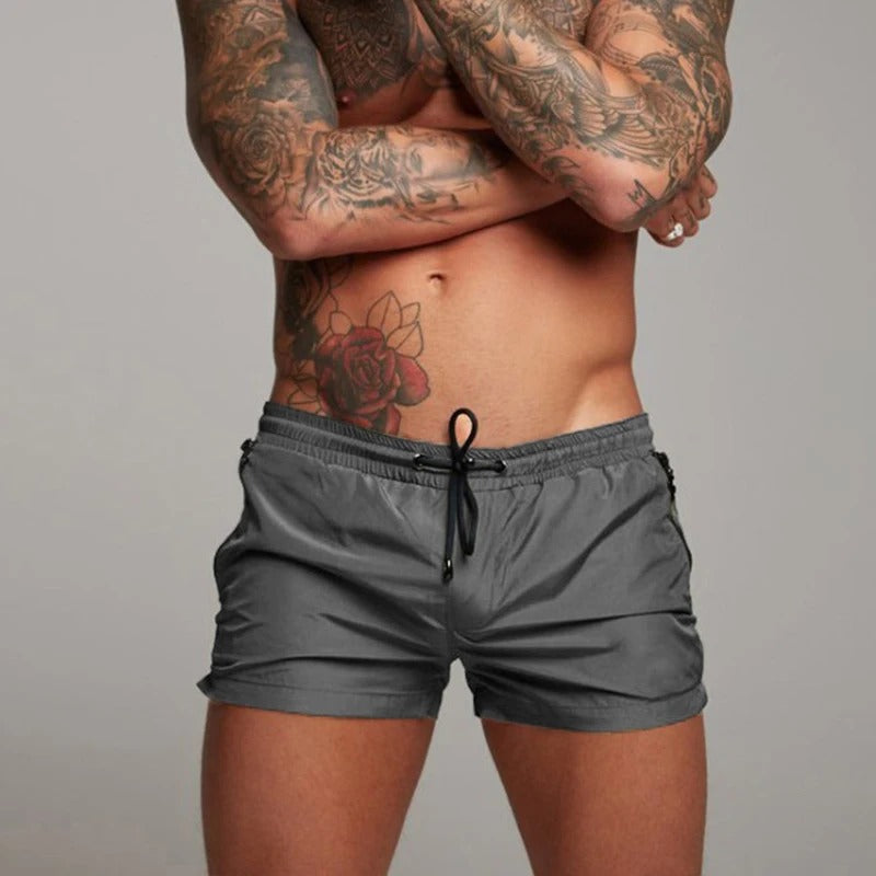 Person wearing grey swim shorts with a plain background