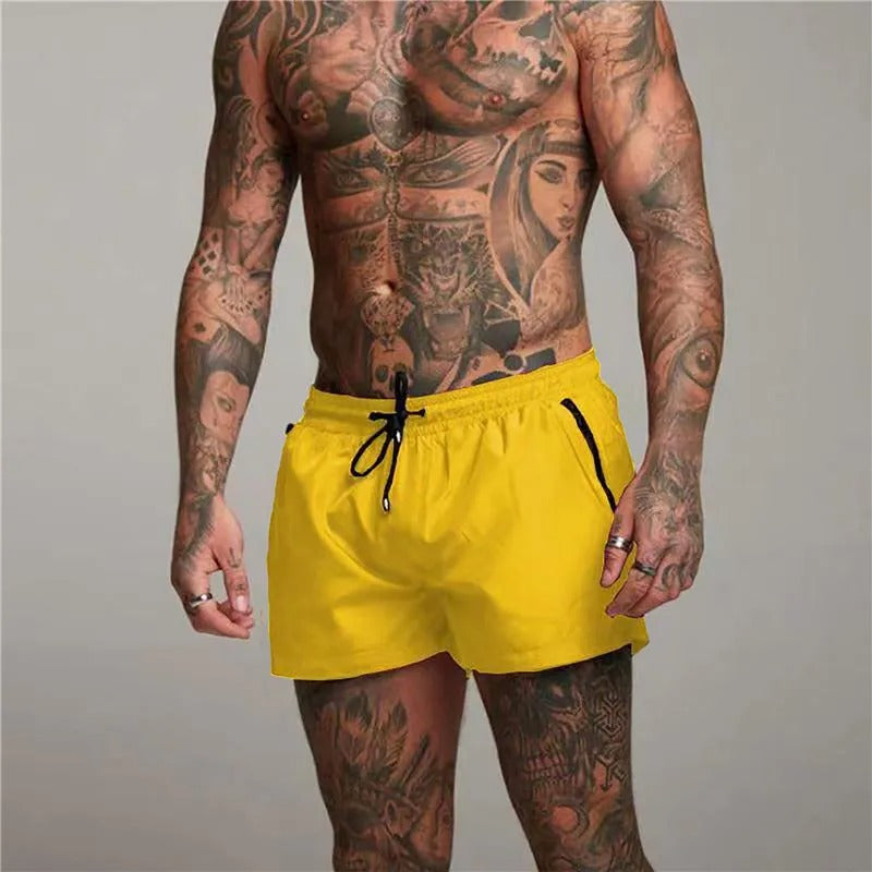Man wearing yellow swim shorts with tattoos on a gray background