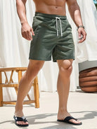 Person wearing green swim shorts standing outdoors with a white curtain in the background