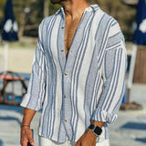 Man wearing a blue and white striped shirt with rolled-up sleeves at a beach.