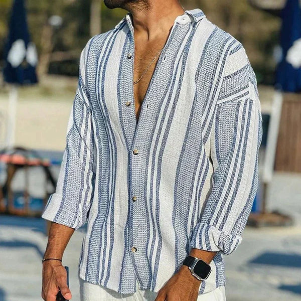 Man wearing a blue and white striped shirt with rolled-up sleeves at a beach.