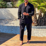 Man wearing a black outfit standing on a wooden deck with plants in the background